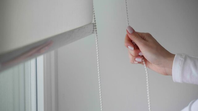 Woman pulling cord to open blinds, closeup