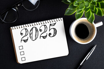 2025 New year resolutions on desk. 2025 goals list with notebook, coffee cup, plant on black table....