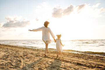 A mother and daughter enjoy a sunny beach stroll, as waves gently lap at their feet during the...