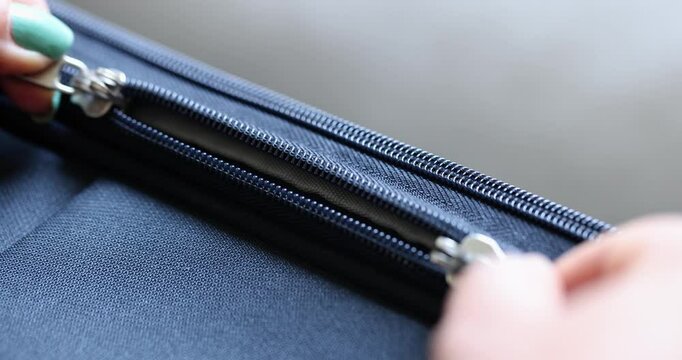 Women's hands open the lock on a zipper on a blue fabric, close-up. Repair of clothes, metal sewing accessories