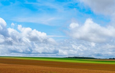 A serene rural landscape featuring fluffy white clouds above lush green fields, illuminated by bright sunlight. This picturesque view captures the beauty and tranquility of nature.