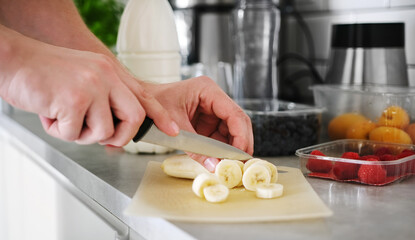 Man Cutting A Banana On The Board With A Knife In The Kitchen