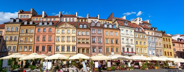 Fototapeta premium Colorful pastel buildings with outdoor seating in the Old Town Square of Warsaw, Poland. The blue sky with white clouds complements the flowers and plants on the buildings, creating a lovely summer