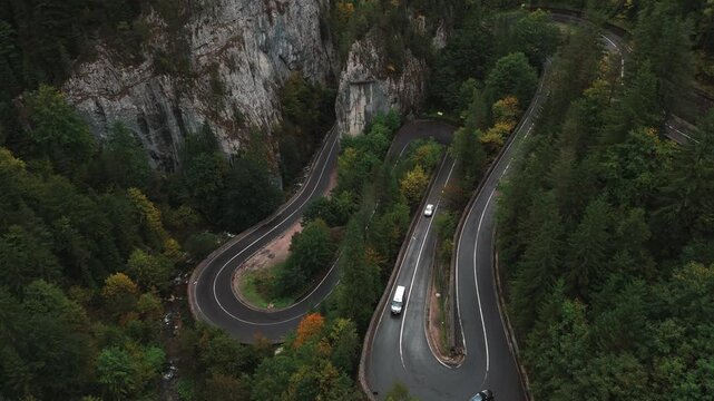 An aerial photograph captures a winding road meandering through lively green forests and dramatic rocky cliffs
