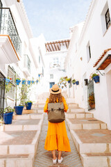 A young traveler woman in a vibrant orange dress and hat enjoys a sunny stroll through a charming...