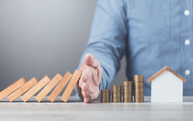 Businessman uses his hand to stop wooden blocks from falling, symbolizing the protection of assets and strategic decision-making in managing resources effectively, domino effect and risk management