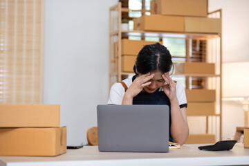 Young Woman Feeling Stressed While Managing Online Sales from Home Surrounded by Packages and Laptop