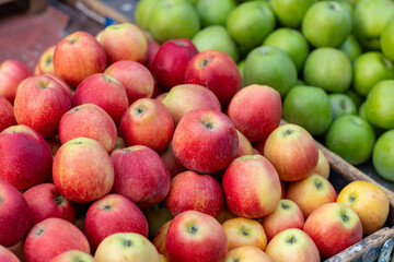 A colorful assortment of ripe red and green apples fills a rustic wooden crate at a bustling farmers' market, inviting shoppers to savor the flavors of autumn.
