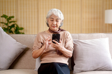 Happy Asian senior elderly old woman using mobile phone receiving news message on smart phone