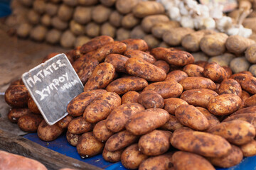 Rows of earthy sweet potatoes fill a market stall, their rich textures and colors drawing attention. A small chalkboard sign labels the Cyprus potatoes, symbolizing local agricultural traditions.