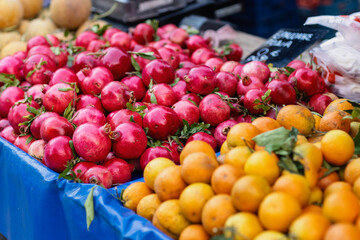 Bright red pomegranates rest alongside vibrant oranges at a bustling market, showcasing the rich colors and enticing variety of fresh fruits available for shoppers to enjoy.
