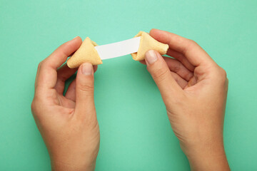 Woman holding tasty fortune cookie and paper with prediction on mint background. Space for text