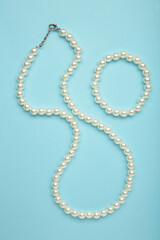 Elegant pearl necklace with bracelet on blue background, top view. Space for text