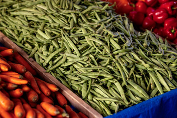 Rows of freshly harvested green beans and bright orange carrots fill the market display, highlighting the seasonal bounty and inviting shoppers to explore local flavors.