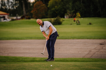 A golfer prepares to putt on the green, focusing intently on the ball. The background includes a...