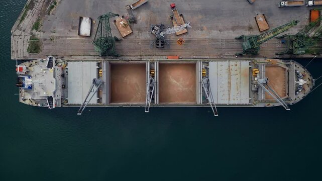 Aerial view of a cargo ship in a harbor uploading grains in a busy port during daylight hours