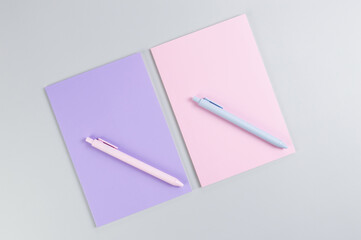 Top view of pink and purple notebooks, pink and blue pens on grey background. School, office wallpaper. Flat lay, copy space.