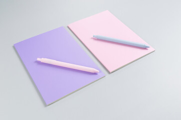 Top view of pink and purple notebooks, pink and blue pens on grey background. School, office wallpaper. Flat lay, copy space.