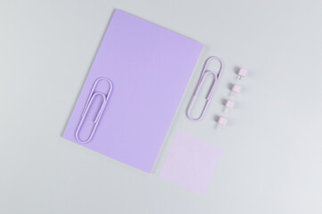 Top view of purple notebook on grey background. Purple sticky note, paperclips and pins. School, office wallpaper. Flat lay, copy space.