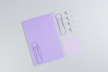 Top view of purple notebook on grey background. Purple sticky note, paperclips and pins. School, office wallpaper. Flat lay, copy space.