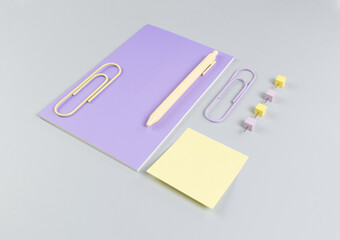 Top view of purple notebook on grey background. Sticky note, paperclips, pen and pins. School, office wallpaper. Flat lay, copy space.