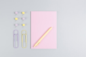 Top view of pink notebook on grey background. Paperclips, pen and pins. School, office wallpaper. Flat lay, copy space.