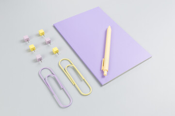 Top view of purple notebook on grey background. Paperclips, pen and pins. School, office wallpaper. Flat lay, copy space.