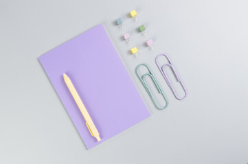 Top view of purple notebook on grey background. Paperclips, pen and pins. School, office wallpaper. Flat lay, copy space.
