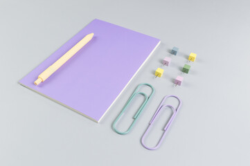 Top view of purple notebook on grey background. Paperclips, pen and pins. School, office wallpaper. Flat lay, copy space.