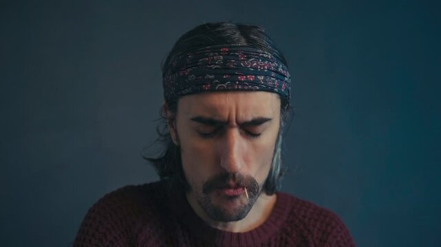 The Charismatic Hippie:rolls a toothpick with his tongue and looks down into the frame long hair. 
toothpick in mouth, mustache, headband, slomo. 
