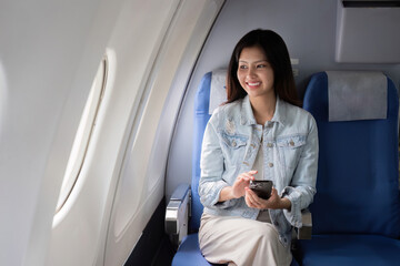 Fototapeta premium Business Woman Traveling in Business Class on a Plane, Using Smartphone, Smiling, Comfortable Seat, Modern Airplane Interior