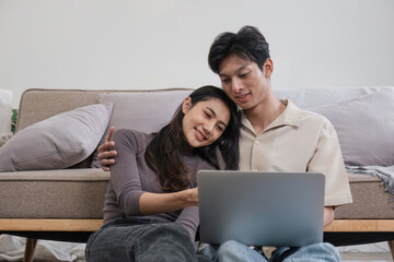 Fototapeta premium Young Couple Relaxing Together on Sofa with Laptop, Enjoying Quality Time at Home in a Modern Living Room