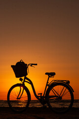 Obraz premium Silhouette of vintage bicycle with a basket on the beach during summer sunset. Copy space. Isolated.