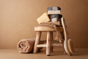 A stack of natural handmade soap bars with a wooden back brush and rolled towel on a rustic wooden...
