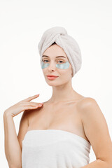 A beautiful woman with blue eyes against a white background, wearing under-eye patches and a towel on her head. This image highlights self-care and the pursuit of a fresh, healthy appearance.