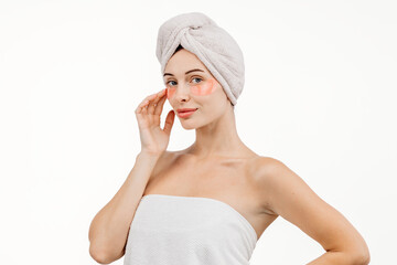 A woman with flawless skin wearing a hair towel after a spa treatment. Her relaxed expression evokes a sense of harmony and self-care against a white background.