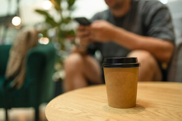 Young man with phone and power bank. Takeaway paper coffee cup with aroma latte coffee on a wood table at city cafe. Male with social media addiction on smartphone scrolling internet, 