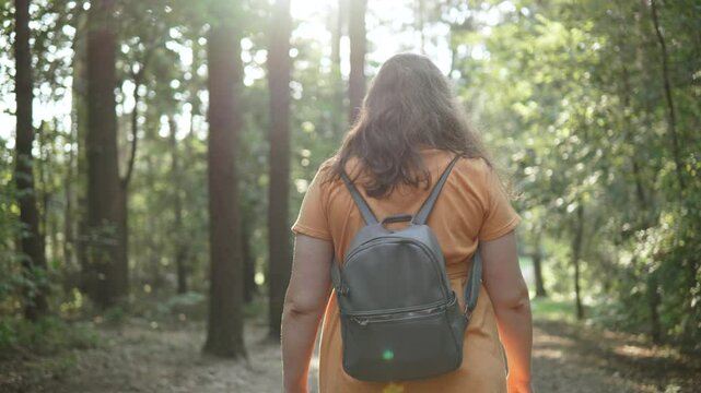 Portrait of happy plus size woman walking with backpack in forest. Young woman turns around and looks at camera with smile.