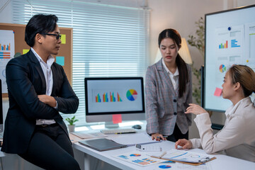 Three people are sitting at a desk with a large monitor in front of them