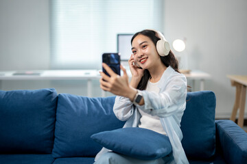 A woman is sitting on a blue couch and taking a selfie with her cell phone