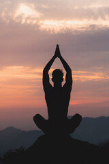 A photo of a silhouette of a man doing yoga and meditation on a mountain top at sunset. 