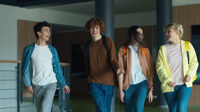Four teenagers friends Caucasian males men guys boys girls women females pupils students walking in corridor university college school jumping happy laugh smiling celebrate end lessons study achieve