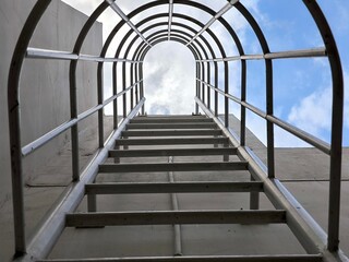 Fototapeta premium Industrial safety ladder. Aluminium cage ladder to enter the roof. Emergency fire escape staircase. Moving forward and motivation concept. A way to be successful life