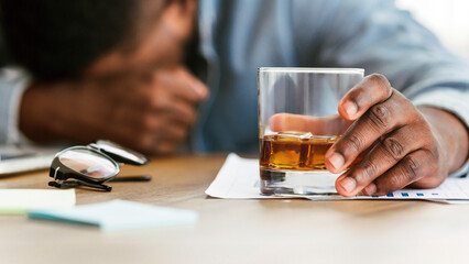 Alcoholism concept. Drunk black employee sleeping at workplace, holding glass with alcohol, panorama