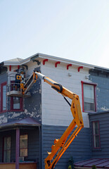 Un homme peignant un vieux bâtiment de ville avec une grue jaune.