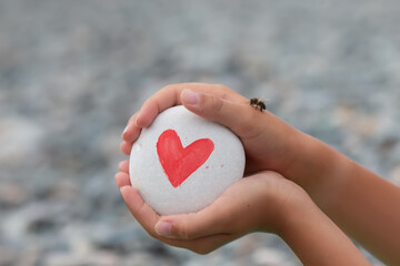 Fototapeta premium The child's hands hold a white stone with a red heart drawn on it.