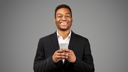 Portrait Of Black Guy Wearing Suit Using Phone Looking At Camera Isolated Against White Background, Panorama