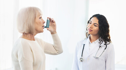 Medical Advice. Elderly woman using asthma inhaler, mexican doctor watching, free space, panorama