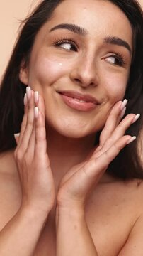 Closeup of a beautiful woman applying moisturizing cream on her face, emphasizing skincare routine and the concept of beauty with a clean, healthy complexion.