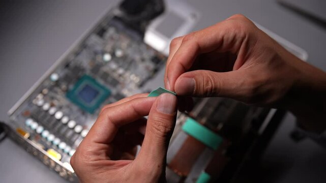 Top view of technician male carefully positioning a new thermal pad on a graphics card, ensuring optimal cooling performance during operation. Concept of computer hardware, repairing, upgrade.